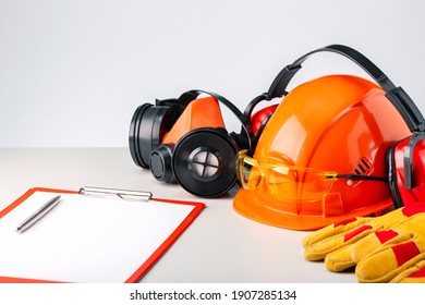 Protective hard hat, headphones, gloves, glasses and clipboard on gray surface.  Construction safety.