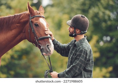 In protective hat. Young man with a horse is outdoors. - Powered by Shutterstock