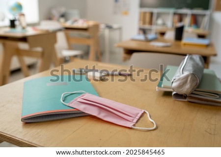 Protective mask on copybook and textile pencilbox on wooden desk in classroom