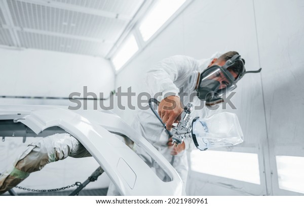 In protective mask. Painting\
the car. Caucasian automobile repairman in uniform works in\
garage.