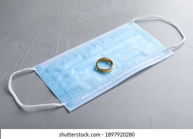 Protective Mask And Wedding Ring On Grey Table. Divorce During Coronavirus Quarantine