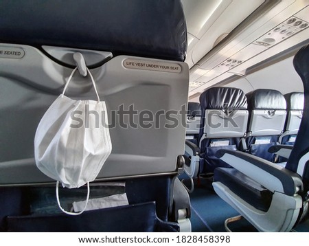 Protective medical white safety mask hanging in airplane for Covid-19, Travel and coronavirus concept close-up