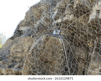 Protective mesh system installed on unstable rock slope to prevent rockfalls and minimize geological hazards. Essential safety measure in landslide prone areas. Protection against mountain collapse