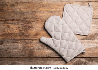 Protective oven glove and potholder on wooden table, top view with space for text - Shutterstock ID 1382633357