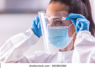 Protective shield adjustment by medical staff worker wearing white overall, blue gloves and disposable facemask.