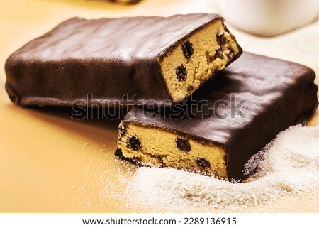 protein bar with sugar-free chocolate and spoonful of casey, whey or creatine in the background. Athletes' food supplementation, macrophotography