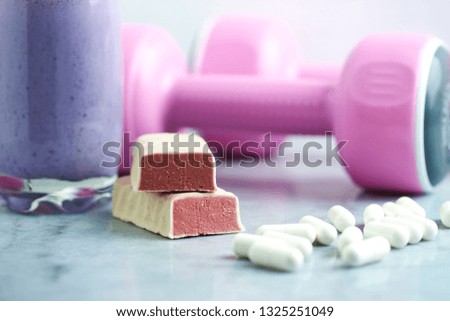 Protein bar in two pieces, Glass of Protein Shake with Milk and Blueberries. Creatine capsules and pink dumbbells in background. Concept for Sport nutrition. Stone / Wooden background. Close up.