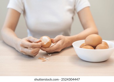 Protein in food, keto diet asian young woman hand peeling, shelling chicken boiled egg, prepares ingredient for breakfast meal on table at home. Removing egg shell, cleaning egg, health care concept. - Powered by Shutterstock