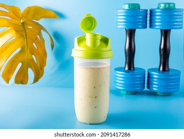 Protein sports shaker. Protein drink and dumbbells. Sports screensaver. Blue background. Front view. - Shutterstock ID 2091417286