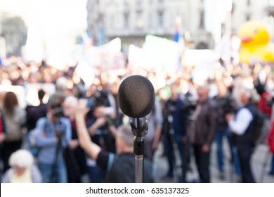 Protest. Political Rally. Demonstration. Microphone In Focus, Blurred Crowd In Background.