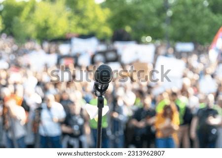 Protest or public demonstration, focus on microphone, blurred crowd of people at political rally in the background
