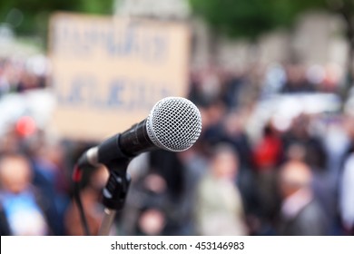 Protest. Public demonstration. Microphone in focus against blurred crowd. Political rally.
