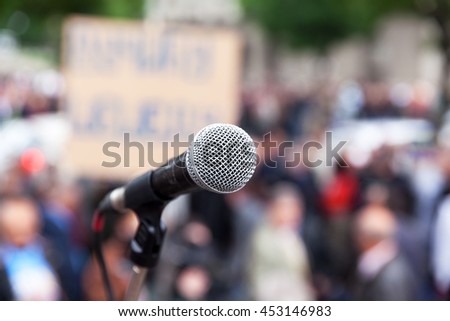 Protest. Public demonstration. Microphone in focus against blurred crowd. Political rally.