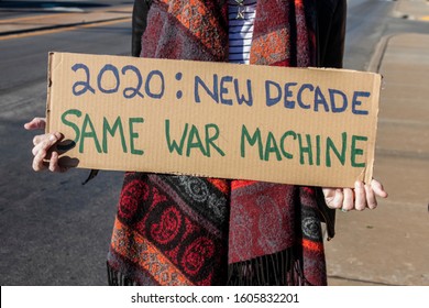 Protest War 2020-New Decade-Same War Machine - woman in scarf holds homemade sign