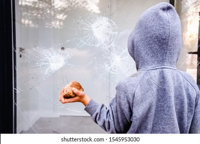 Protester Holding A Rock To Break The Glass Of A Shop Window In The Street During Protests.