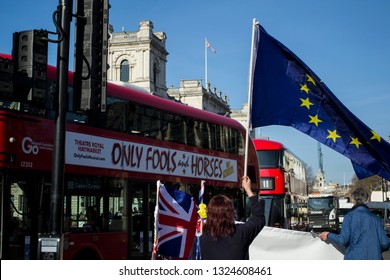 A protester waving a European Union flag in front of Palace of Westminster. A bus is passing by with a musical banner name 'Only Fools and Horses'. The picture is taken at London on 22/02/2019