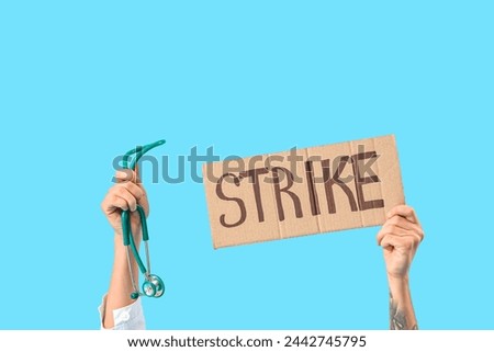 Protesting male doctor holding placard with word STRIKE and stethoscope on blue background