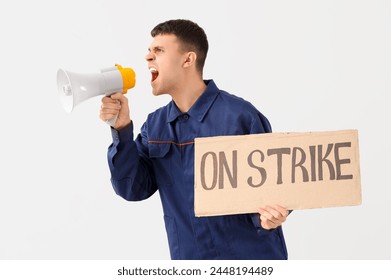 Protesting mechanic shouting into megaphone and holding placard with text ON STRIKE against light background