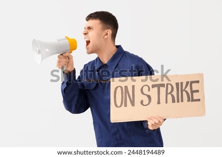 Protesting mechanic shouting into megaphone and holding placard with text ON STRIKE against light background