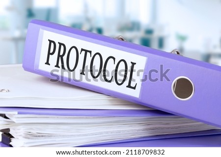 Protocol, text written in a folder with documents in trendy purple color, lying on a stack of papers, documents on an office table, against a background of soft blur office background. 
