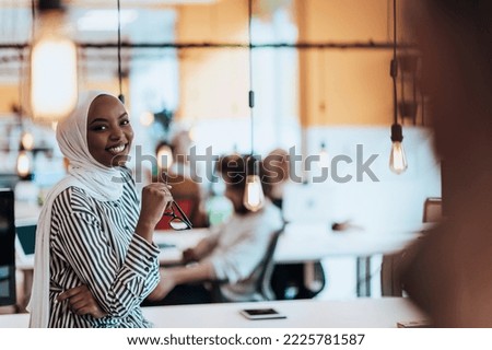 Protrait of a black ( african-american) female muslim standing in a modern business office while wearing a hijab.