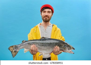 Proud bearded fisherman having glad expression catching big fish having successful day. Handsome male with blue eyes dressed casully came home after going fishing bringing huge trout for supper - Powered by Shutterstock