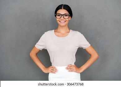 Proud Of Being Herself. Smiling Young Businesswoman Holding Hands On Hips And Looking At Camera While Standing Against Grey Background