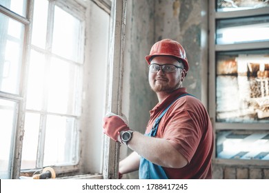 Proud builder in uniform is carefully working with a window at a construction site - Powered by Shutterstock