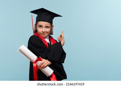 Proud child girl in graduate suit with certificate diploma on light blue background looking at camera, showing promo, pointing finger up, grinning, inviting use link. Graduate Celebrating Graduation. - Shutterstock ID 2146197419