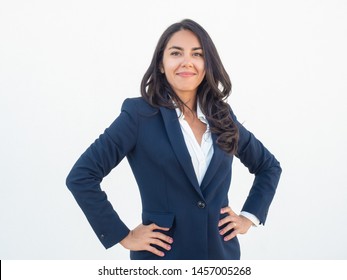 Proud Confident Business Woman Posing Over White Background. Happy Beautiful Young Latin Woman In Office Suit Placing Hands On Hip, Looking At Camera And Smiling. Business Success Concept