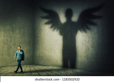 Proud And Confident Young Businessman Casting A Superhero Shadow With Angel Wings On A Dark Room Wall. Inner Power, Ambition And Leadership Concept.