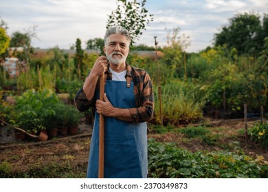 Proud elderly gardener posing for the camera while standing and holding a shovel he uses to work in his garden - Powered by Shutterstock