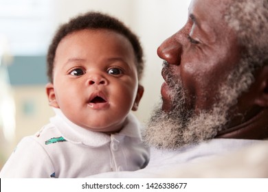Proud Grandfather Cuddling Baby Grandson In Nursery At Home