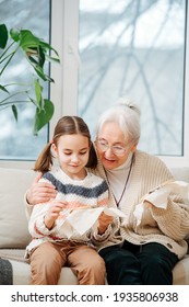 Proud granny sitting on a couch with her granddaughter. they are embroidering on a loop together. She's hugging and encouraging her.