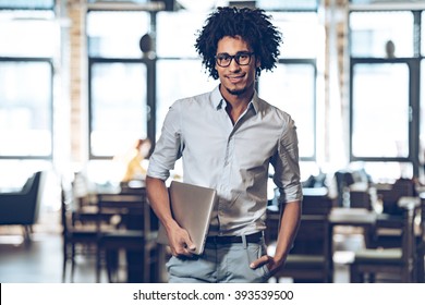 Proud With His Small Business. Young Cheerful African Man Carrying Laptop And Looking At Camera With Smile While Standing At Cafe