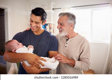 Proud Hispanic father holding his four month old son at home, grandfather standing beside them