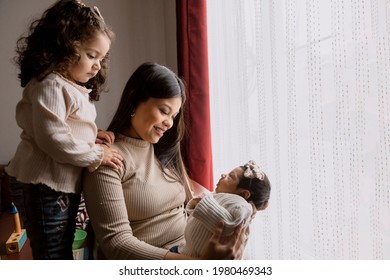 Proud Hispanic Mom Holding Her Newborn Baby - Latin Mother And Daughters At Home. Toddler Kid Meeting New Sibling