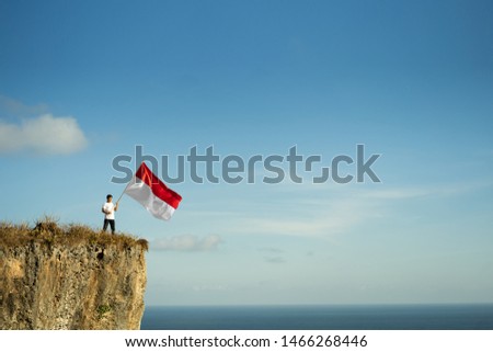 proud indonesian man on a beach cliff raising red and white indonesia flag