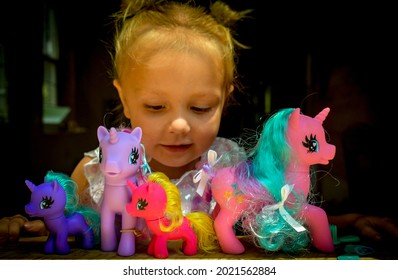 A proud little girl smiling and playing with my little pony unicorn toys she received for a birthday gift- with the sun shinning on her