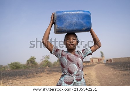 Proud looking African girl walking from her parents' isolated home to the distant village well, carrying a water canister on her head; human right to safe drinking water and sanitation concep
