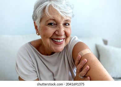 Proud Mature Woman Smile After Vaccination With Bandage On Arm. Beautiful Smiling Senior Woman 70s After Receiving The Coronavirus Vaccine. Elderly Lady Getting Immunization Via Anti-viral Vaccine.