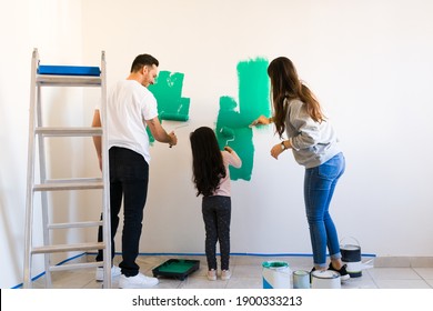 Proud Mom And Dad Telling Their Daughter She Does A Good Job At Painting The Walls. Family Renovating Together Their New Home