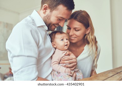 Proud Mother And Father Smiling At Their Newborn Baby Daughter At Home