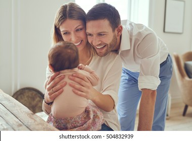 Proud Mother And Father Smiling At Their Newborn Baby Daughter At Home