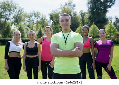 I Am Proud Of My Team! Group Of  Athletic Young Women In Sportswear Standing Together In Line, Looking At Camera And Smiling In Green Summer Park  Outdoors, Coach In Foreground