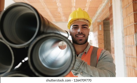 Proud People Working In Construction Site. Portrait Of Happy White Man At Work In New House. Professional Latino Worker Carrying Pipes And Smiling At Camera