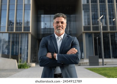 Proud portrait of older senior businessman professional ceo, coach, leader looking at camera near office. Smiling confident latin hispanic mature business man standing crossed arms on busy city street