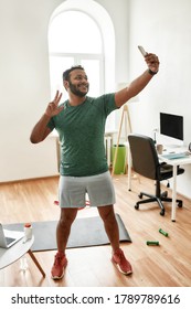 Proud Of The Result. Full Length Shot Of Excited Active Man Holding Smartphone, Showing Victory Sign While Taking A Selfie During Morning Workout At Home. Fitness, Motivation Concept. Vertical Shot