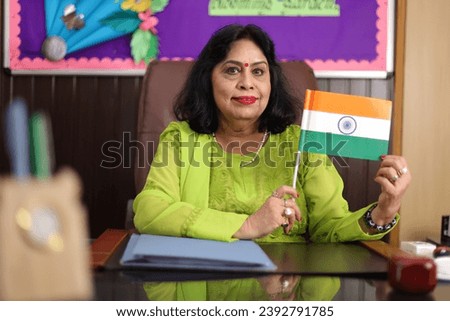 Proud school principal showcasing Indian flag confidently sitting in her office. looking into the camera.