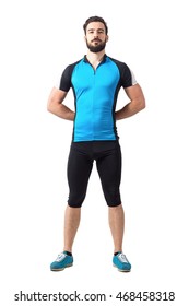 Proud strong sporty cyclist in cycling clothes standing with hands hands behind back. Full body length portrait isolated over white studio background.